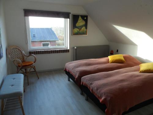 two beds in a room with a window and a chair at Logi i hus med kunst og have in Vestervig