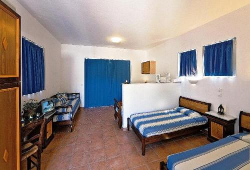 a room with two beds and a kitchen with blue curtains at Katikies Studios & Apartments in Lardos