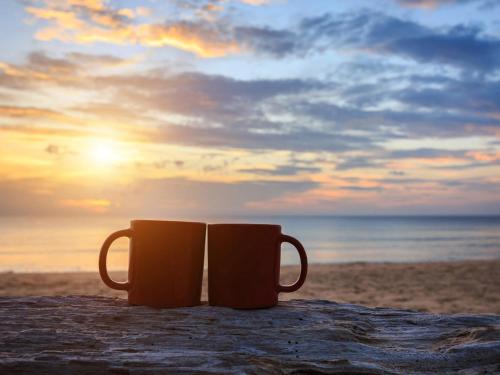 two coffee mugs sitting on the beach at sunset at All the Tides - Between Tides in Margate