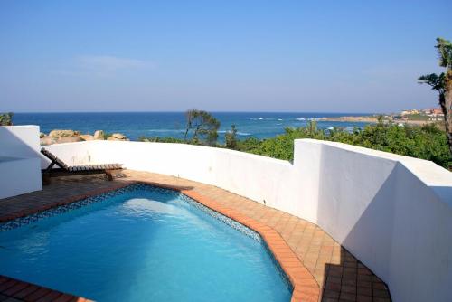 a swimming pool next to a white wall and the ocean at Rosscarbery 6 in Margate