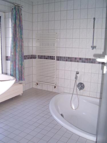 Baño de azulejos blancos con bañera y lavamanos en Apart Hotel Taucha en Taucha