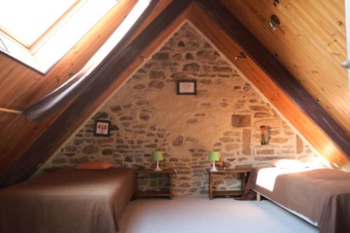 Cette chambre mansardée comprend 2 lits et un mur en pierre. dans l'établissement Les Gîtes Aux Volets Roses, à Landunvez