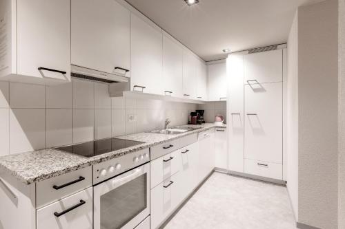 a white kitchen with white cabinets and a sink at Belmont- Apartment Haus in Arosa
