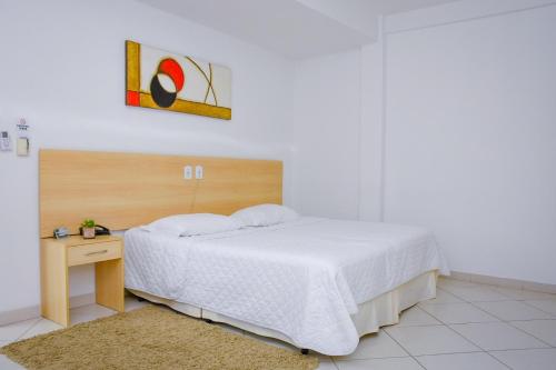 a bedroom with a white bed and a wooden headboard at Pioneiro Hotel in Teixeira de Freitas
