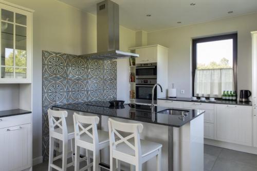 a kitchen with white cabinets and a counter with stools at Hotel SPA Dr Irena Eris Wzgórza Dylewskie - Siedliska in Wysoka Wieś