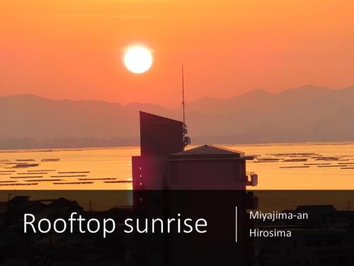 a sunset over the ocean with a building in the foreground at Ryokan with natural hot springs and okonomiyaki Miyajima-an Hiroshima in Miyajima