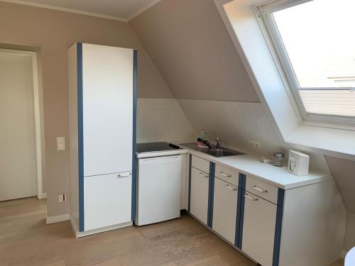 eine Küche im Dachgeschoss mit weißen Schränken und einem Fenster in der Unterkunft Haus Kamp in Tinnum