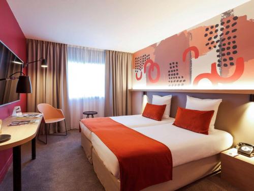 シャルボニエール・レ・バンにあるメルキュール リヨン シャルボニエールの大きなベッドとデスクが備わるホテルルームです。