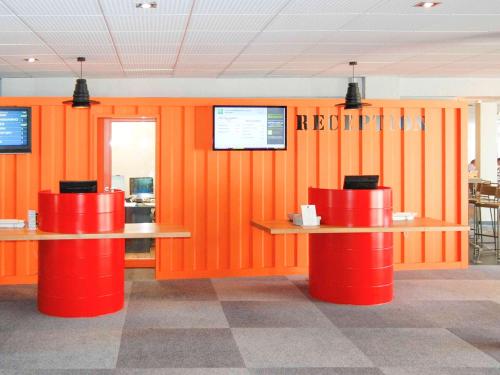 un restaurant avec des murs orange et 2 tables rouges dans l'établissement ibis Styles Marseille Aéroport, à Vitrolles