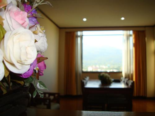 a vase of flowers on a table with a window at Chiang Mai Phucome Hotel in Chiang Mai