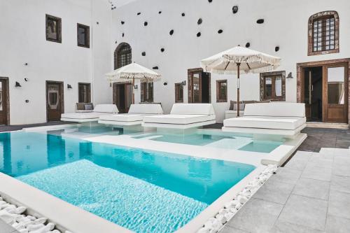 an indoor pool with white furniture and umbrellas at Winery Hotel 1870 in Fira