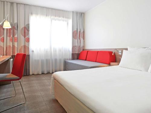 a hotel room with a bed and a red chair at Novotel Poznań Malta in Poznań