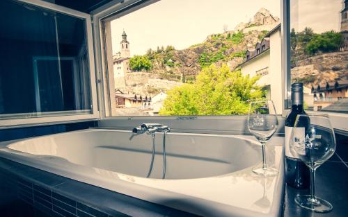 a bath tub with two wine glasses and a window at Chambre d'hôte Valère in Sion