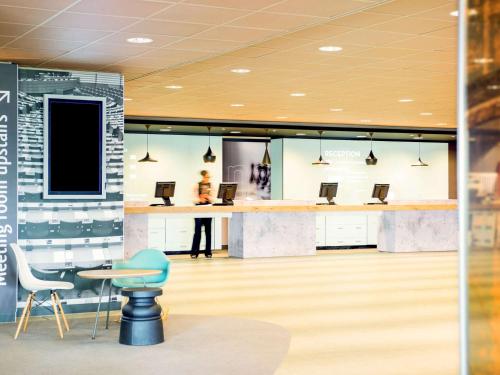 a lobby with a desk and chairs and a person at Ibis Schiphol Amsterdam Airport in Badhoevedorp