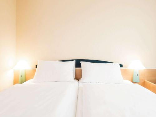 two beds in a room with white sheets and lamps at ibis Paderborn City in Paderborn