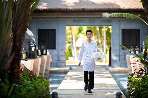 a man in a white lab coat walking down a sidewalk at Raffles Hainan Clear Water Bay in Sanya