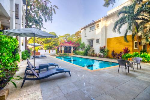 a swimming pool with chairs and an umbrella next to a building at Rainforest - Casa Del Sol, Anjuna - 3 kms from the beach in Anjuna