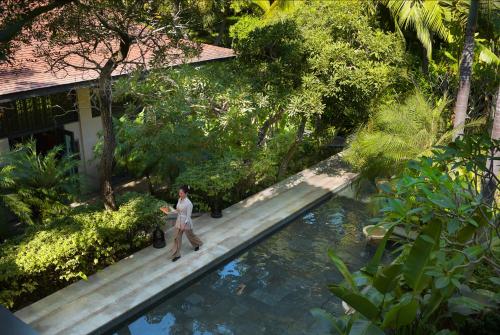 a man walking on a wooden path next to a swimming pool at Raffles Hainan Clear Water Bay in Sanya