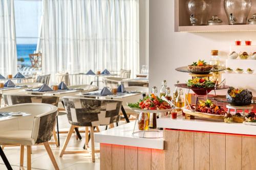 a restaurant with tables and chairs with food on a counter at King Jason Protaras - Designed for Adults by Louis Hotels in Protaras
