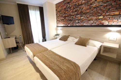 a hotel room with a large bed and a brick wall at Hotel Alda San Carlos in Santiago de Compostela