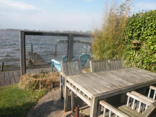 a wooden table and chairs sitting next to a body of water at The Outpost Lakehouse- enjoy our house at Reeuwijkse Plassen - near Gouda in Reeuwijk