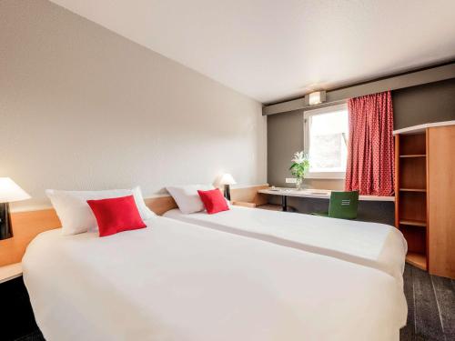een hotelkamer met 2 grote bedden met rode kussens bij ibis Lourdes Centre Gare in Lourdes