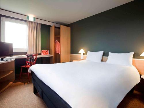 um quarto de hotel com uma grande cama branca e uma secretária em Ibis Provins em Provins