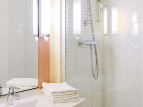 uma casa de banho com um chuveiro e toalhas num lavatório em Hôtel Ibis Nevers em Nevers