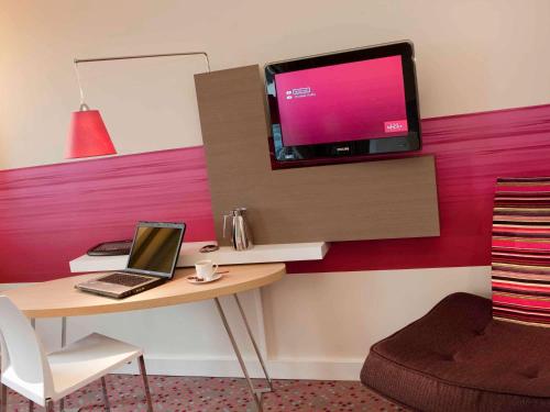 a desk with a laptop and a tv on a wall at Mercure Paris Orly Rungis Aéroport in Rungis