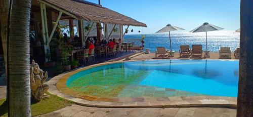 a swimming pool at a resort with the ocean in the background at Tauch Terminal Resort Tulamben & Spa in Tulamben