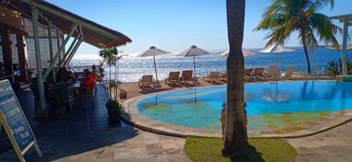 a swimming pool next to the ocean with chairs and umbrellas at Tauch Terminal Resort Tulamben & Spa in Tulamben