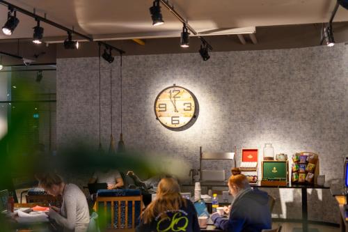 people sitting at tables in a restaurant with a clock on the wall at Skotel The Hague, Hotelschool The Hague in Scheveningen