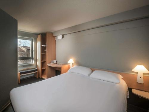 um quarto com uma grande cama branca e uma janela em ibis Carcassonne Centre - La Cité em Carcassonne