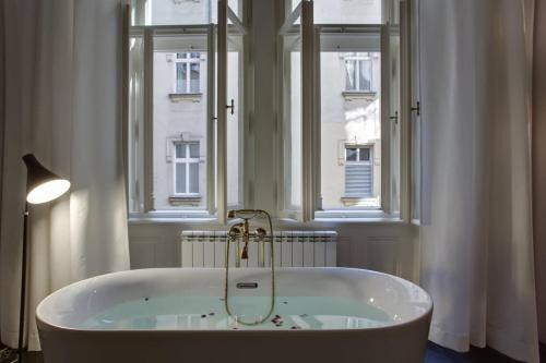 een badkamer met een bad en 2 ramen bij BRIGHT Prague Havelská in Praag