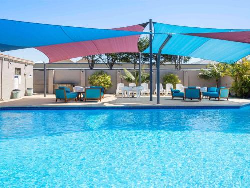 a swimming pool with blue chairs and a blue umbrella at ibis Styles Geraldton in Geraldton