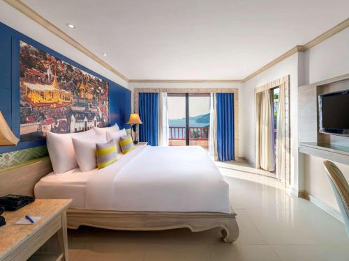 um quarto com uma grande cama branca e uma televisão em Novotel Phuket Resort em Praia de Patong