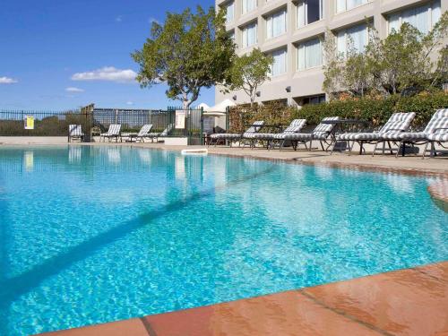 a large swimming pool with chairs and a building at Mercure Sydney Parramatta in Sydney