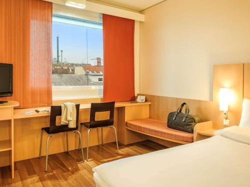 Pokój hotelowy z biurkiem, łóżkiem i oknem w obiekcie Ibis Wien Messe w Wiedniu