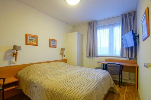 Habitación de hotel con cama, escritorio y ventana en Appartementen Zeezicht - 3 en Katwijk aan Zee