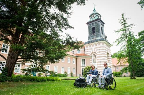 a man and a woman in a wheelchair in front of a building at Heidehotel Bad Bevensen in Bad Bevensen
