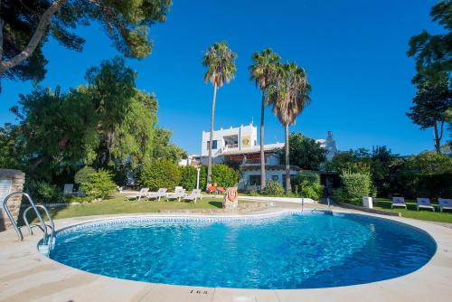 a swimming pool with palm trees and a building at Suites Cortijo Fontanilla in Conil de la Frontera