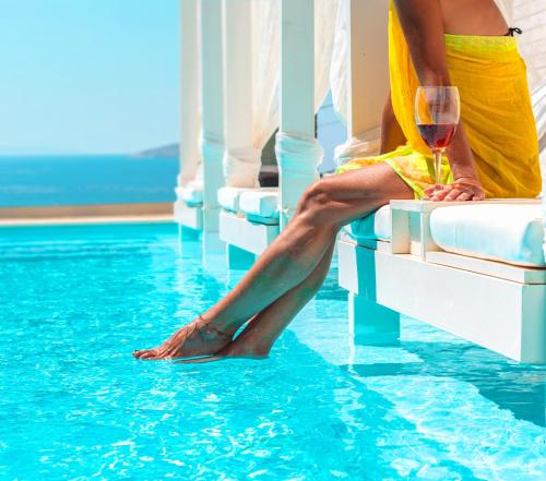 een vrouw in een gele jurk zittend in een zwembad met een glas wijn bij Andros Luxury House in Kypri
