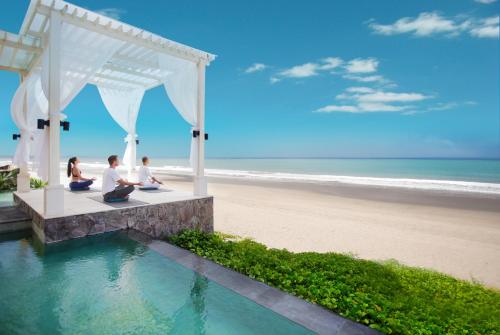 a group of people sitting on a bench at the beach at The Seminyak Beach Resort & Spa in Seminyak