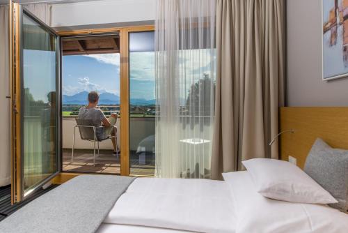 a man sitting in a chair on the balcony of a bedroom at Hotel-Restaurant Ammerhauser in Anthering