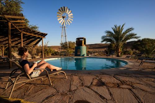 een vrouw in een stoel naast een zwembad met een windmolen bij Canyon Roadhouse Campsite in Karasburg