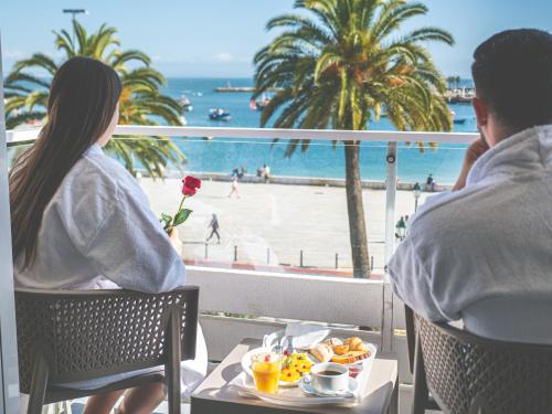 
two people sitting at a table in front of a beach at Hotel Baia in Cascais
