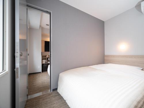 a bedroom with a white bed and a sliding glass door at Super Hotel Okayama Station Higashiguchi in Okayama