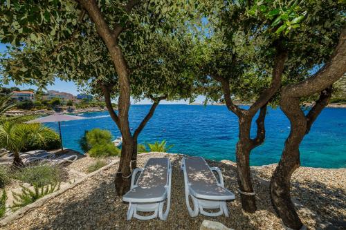 two lounge chairs under trees next to the water at Villa Lavanda Deluxe in Rogoznica