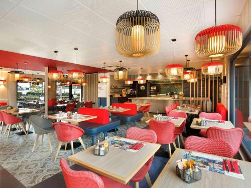 a restaurant with red chairs and tables and chandeliers at ibis Le Mans Est Pontlieue in Le Mans