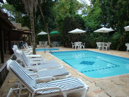 a swimming pool with lounge chairs and umbrellas next to it at Pousada Y-Goá in Bertioga